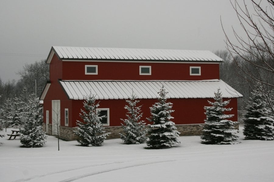 Red two-story steel building with a light metal roof and stone wainscot, surrounded by snow-covered evergreens.